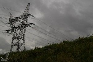 Electricity tower behind a green hill with a gray sky